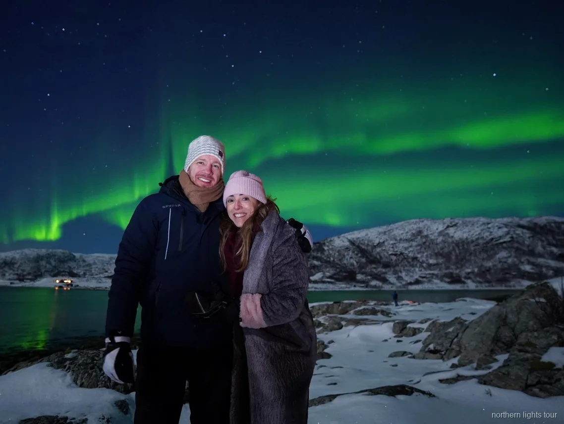 Petit groupe observant l'aurore boréale depuis un campement au bord d'un fjord sur l'excursion chasse de Tromsø