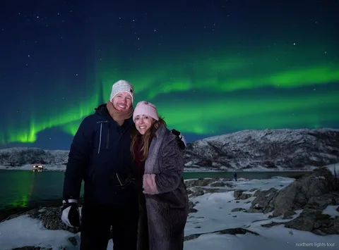 Lille gruppe ser nordlyset fra en fjordlejr på Tromsø nordlysjagt-tur