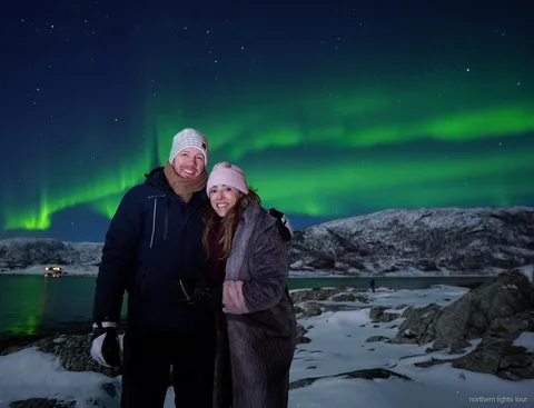 Mindre grupp betraktar norrskenet från ett fjordläger på Tromsø norrskenjakt-tur