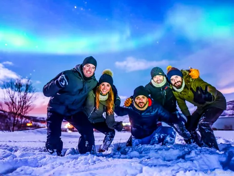 Grupa na Tromsø Safari na zorzę polarną obserwująca aurorę z obozu przy ogrzewanym autobusie